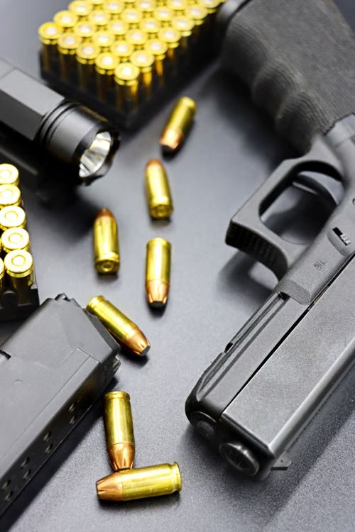 A black handgun, magazines and brass-colored cartridges rest on a dark surface.